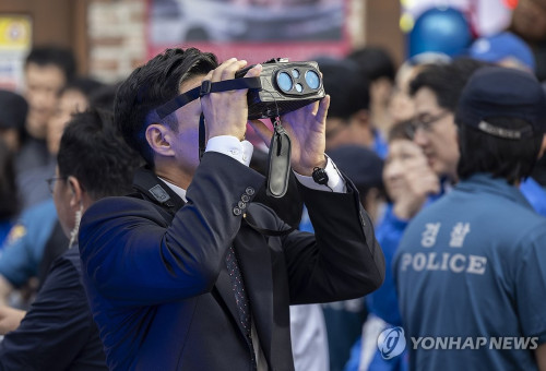 경남 거제시에서 열린 더불어민주당 이재명 대선후보 유세에서 경호에 나선 경찰이 특수 쌍안경을 이용해 주변 건물의 움직임을 살피고 있다.